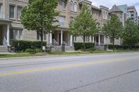 an empty street and some buildings on both sides of the road, with the green grass between the two trees