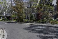 an empty city street lined with parked cars and trees in front of the houses on the right side