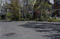 an empty city street lined with parked cars and trees in front of the houses on the right side