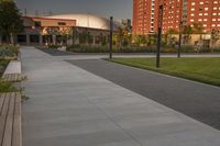 a city street surrounded by grass and tall buildings at the end of a street there is a paved pathway in front of the building