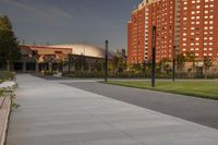 a city street surrounded by grass and tall buildings at the end of a street there is a paved pathway in front of the building