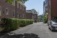 a car is parked on a paved side walk near a tree and brick building on the opposite side