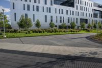 a city street surrounded by grass and tall buildings at the end of a street there is a paved pathway in front of the building