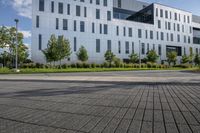 a city street surrounded by grass and tall buildings at the end of a street there is a paved pathway in front of the building