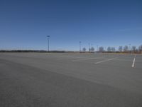 an empty parking lot with two traffic lights in the distance and tall poles in the middle