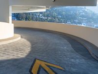 a parking lot with a yellow arrow on the concrete floor near a house in a mountainous area