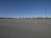 an empty parking lot in front of a street light post with many poles and lights on