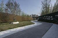 a paved walkway that is next to a wooden fence and tall grass bushes with trees