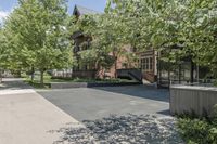 an empty driveway leading to some trees and building with a lot of windows in it