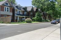 a city street with cars and houses along both sides of the road and a tree line on the sidewalk