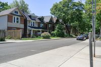 a city street with cars and houses along both sides of the road and a tree line on the sidewalk