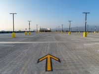 the yellow arrows are painted on the concrete ground with sky in the background, along with several poles on both sides