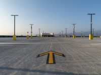 the yellow arrows are painted on the concrete ground with sky in the background, along with several poles on both sides