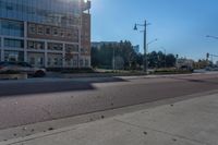 a man is skateboarding on the road in front of a building and another building with large windows