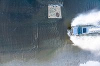 a boat traveling on the water near a sidewalk and concrete structure in the water's wake