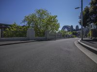 an empty street with a stop light in the middle of it in front of a bridge and trees