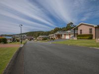 a very street with several houses and a hill in the background with green grass, bushes, and other homes