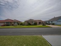 a row of houses on a residential street with grass around and an empty sidewalk at the front and the end