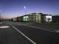 a roadway with a parking lot next to an office building at night time time in a deserted city