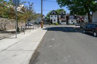 there is a street that looks very quiet with cars parked and trees in front of it