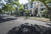 an empty street with buildings in the background and trees on both sides of the street