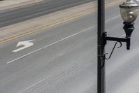 a street light sitting by a white arrow in the middle of a road next to a paved road