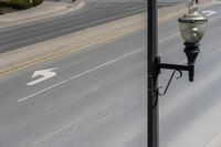 a street light sitting by a white arrow in the middle of a road next to a paved road