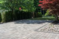 a brick walkway leading up to a driveway lined with trees and shrubs outside of a house