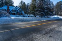 there are snow on the ground and the street is empty outside of the house, with trees lining the front of the house behind it