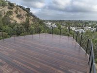 wooden deck with metal railing on residential terrace overlooking city skyline with trees in back ground