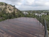 wooden deck with metal railing on residential terrace overlooking city skyline with trees in back ground