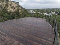 wooden deck with metal railing on residential terrace overlooking city skyline with trees in back ground