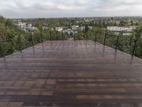 wooden deck with metal railing on residential terrace overlooking city skyline with trees in back ground