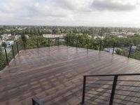 wooden deck with metal railing on residential terrace overlooking city skyline with trees in back ground