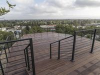 wooden deck with metal railing on residential terrace overlooking city skyline with trees in back ground