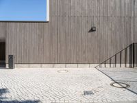 a skateboard sitting on the pavement near a fence in front of a building with a wooden wall