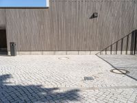 a skateboard sitting on the pavement near a fence in front of a building with a wooden wall