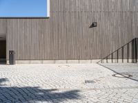 a skateboard sitting on the pavement near a fence in front of a building with a wooden wall