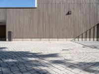 a skateboard sitting on the pavement near a fence in front of a building with a wooden wall