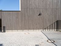 a skateboard sitting on the pavement near a fence in front of a building with a wooden wall