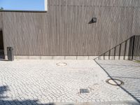 a skateboard sitting on the pavement near a fence in front of a building with a wooden wall