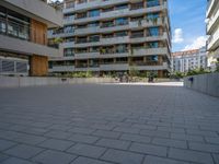 an open courtyard area in front of a residential building with apartments behind it on a clear day