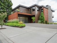 a driveway with trees and green shrubs and house in background on a cloudy day with grey sky