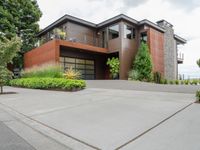 a driveway with trees and green shrubs and house in background on a cloudy day with grey sky