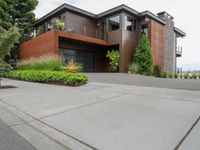 a driveway with trees and green shrubs and house in background on a cloudy day with grey sky