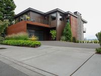 a driveway with trees and green shrubs and house in background on a cloudy day with grey sky