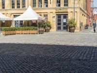 an empty building with two white umbrellas in front of it and some tables outside