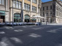 tables of several people on the side of an empty street and buildings with open windows