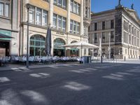 tables of several people on the side of an empty street and buildings with open windows