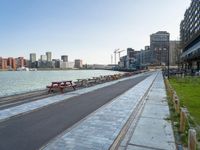 a bench is next to a city river as people walk by the shore line and some buildings